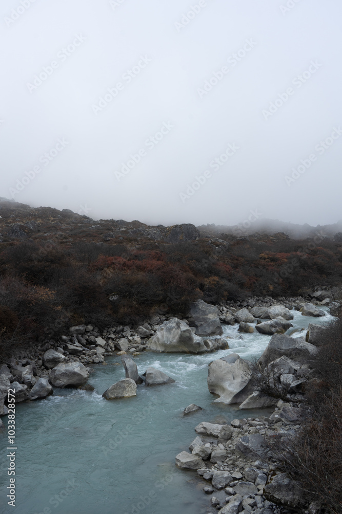 A misty river flows through rocky terrain with sparse vegetation.