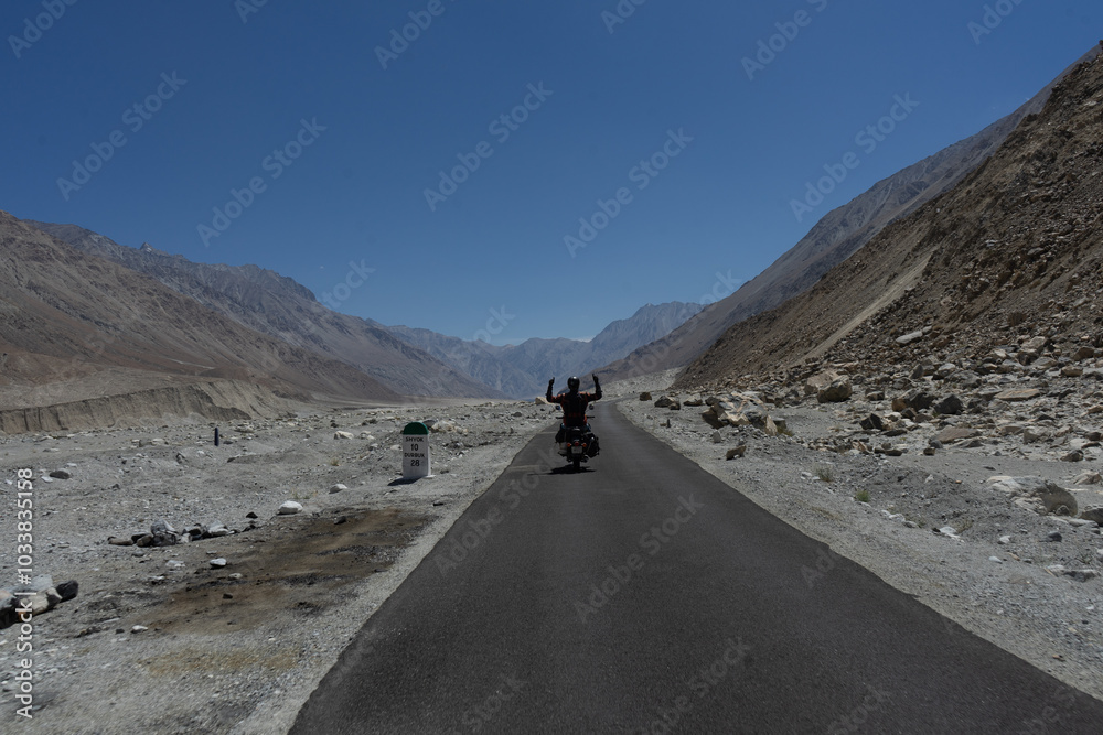 A motorcyclist on a scenic mountain road under a clear blue sky A motorcyclist on a scenic mountain road under a clear blue sky