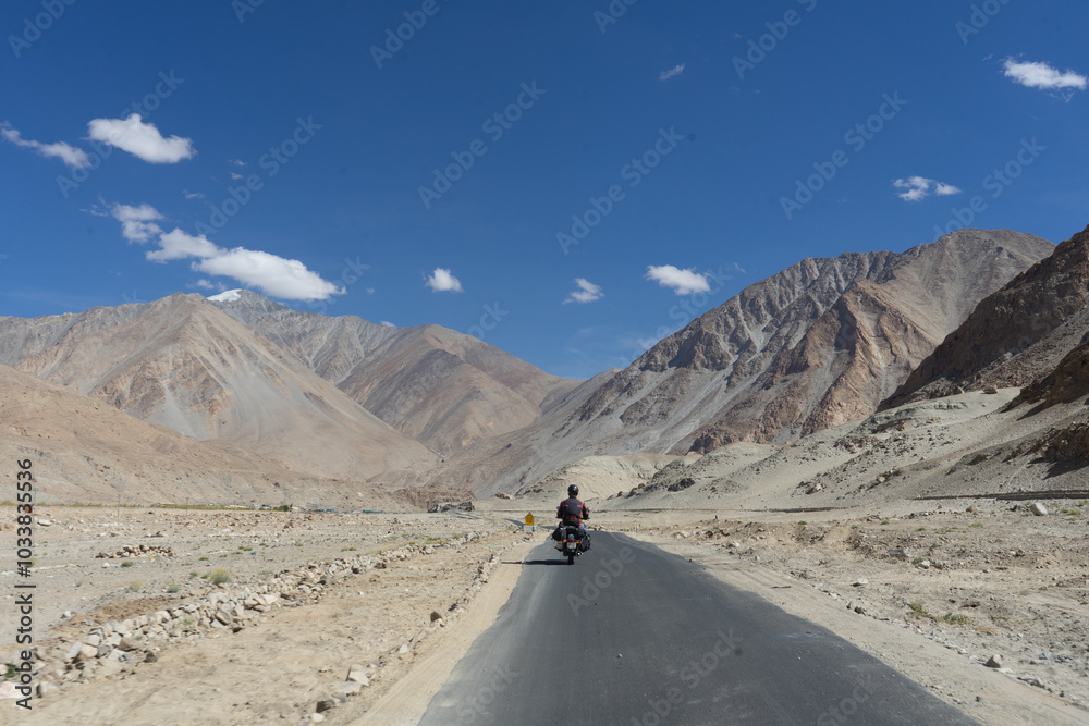Motorcyclist riding on a remote mountain road under a clear blue sky Motorcyclist riding on a remote mountain road under a clear blue sky