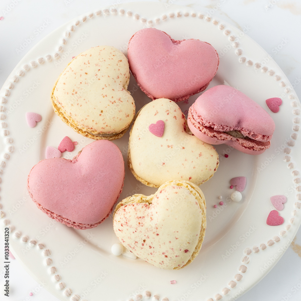French sweet cookies macarons macaroons with color sprinkles on retro plate on marble table background. Heart shape macaron and decor. French sweet cookies macarons macaroons with color sprinkles on retro plate on marble table background. Heart shape macaron and decor.