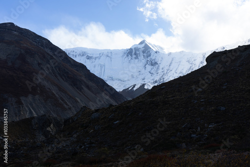 A majestic snowy mountain peak towers over a rugged valley under a clear sky.