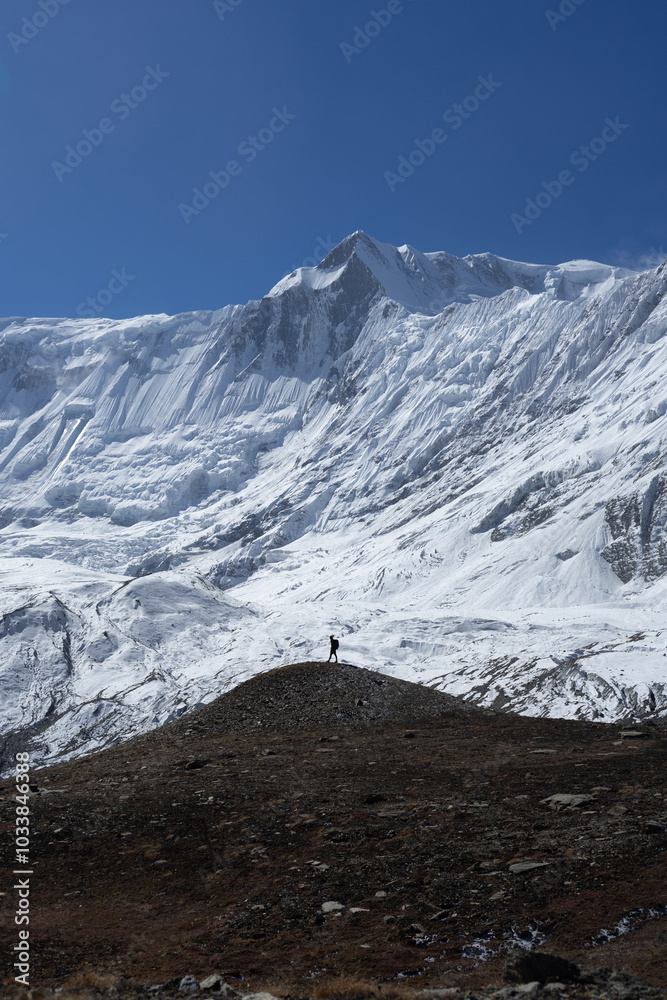 Fototapeta premium A lone hiker standing on a small hill with a backdrop of majestic, snow-capped mountains.
