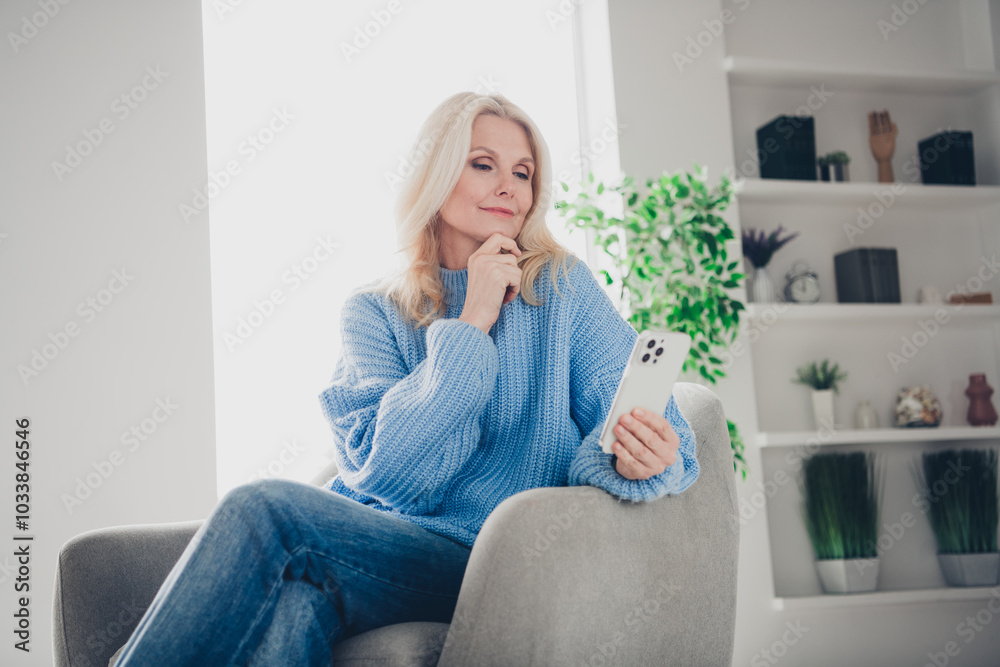 Photo of pretty aged woman sit chair use phone think wear pullover free time modern apartment indoors Photo of pretty aged woman sit chair use phone think wear pullover free time modern apartment indoors