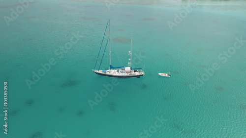 Photography Aerial view of sailboat yacht with dinghy anchored in the turquoise clear water ocean lagoon