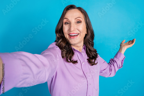 Photo of charming positive woman wear violet shirt recording video showing arm empty space isolated blue color background