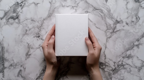 An 8K resolution, photorealistic image of hands gently supporting a plain white book against a background of richly veined marble