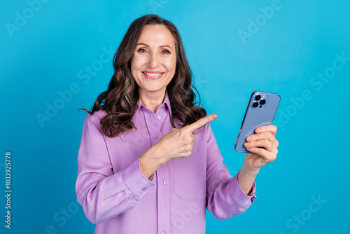 Photo of adorable lovely woman wear violet shirt pointing finger modern device empty space isolated blue color background