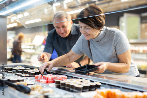 Husband and wife choose fresh delicious japanese rolls together in the grocery section of supermarket photo