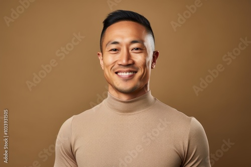 Portrait of a blissful asian man in his 30s showing off a lightweight base layer in front of soft brown background photo