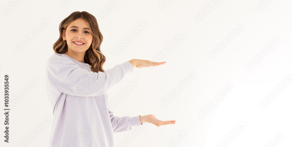 Young confident woman showing logo on empty space between arms. Smiling girl inviting or advertising promo deal, pointing hands right and looking at camera, white background. Young confident woman showing logo on empty space between arms. Smiling girl inviting or advertising promo deal, pointing hands right and looking at camera, white background.