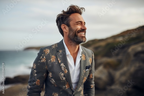 Portrait of a smiling man in his 30s dressed in a stylish blazer while standing against serene seaside background