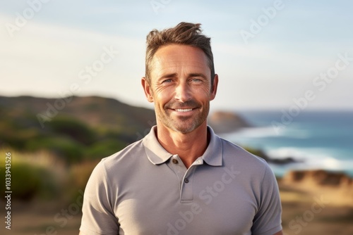 Portrait of a smiling man in his 40s wearing a breathable golf polo isolated on serene seaside background