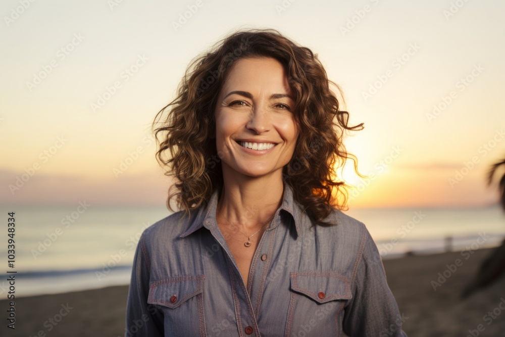 Portrait of a grinning woman in her 40s sporting a versatile denim shirt on stunning sunset beach background