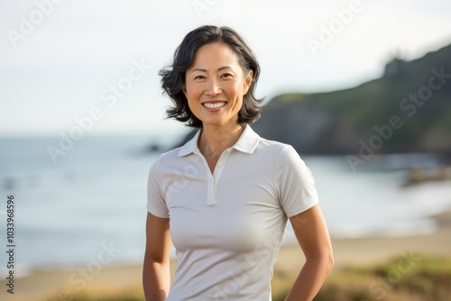 Portrait of a grinning asian woman in her 40s wearing a breathable golf polo over calm bay background