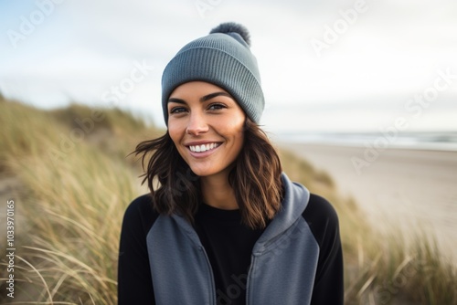 Portrait of a smiling woman in her 30s sporting a trendy beanie isolated in serene dune landscape background