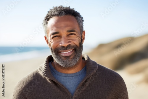 Portrait of a satisfied afro-american man in his 50s wearing a cozy sweater while standing against serene dune landscape background