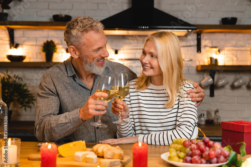 Happy married couple celebrating special event during the romantic dinner in the kitchen while clinking toasting cheering wine glasses. Love and relationship concept photo