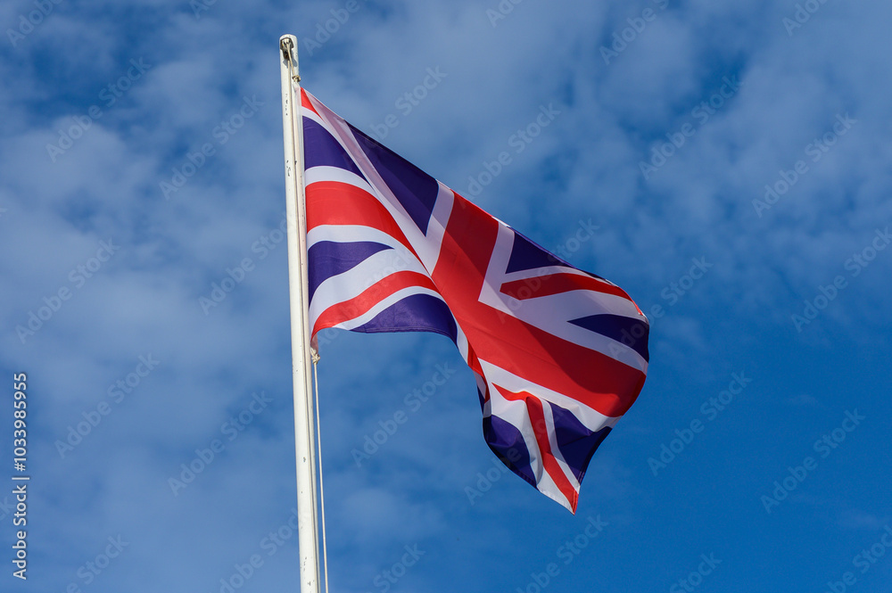 Fototapeta premium British flag waving under a clear blue sky during a sunny day in the United Kingdom