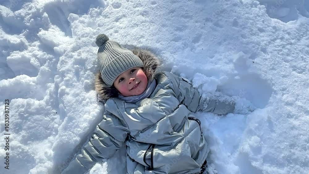 Cheerful little girl in in snowsuit enjoying lying in the snow. A portrait of cute little baby girl having fun outdoor in winter. Happy child girl plays with a snow in winter day. Cheerful little girl in in snowsuit enjoying lying in the snow. A portrait of cute little baby girl having fun outdoor in winter. Happy child girl plays with a snow in winter day.