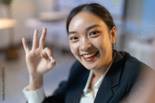 Confident young asian businesswoman in an office, smiling and showing an ok sign, radiating success and professionalism