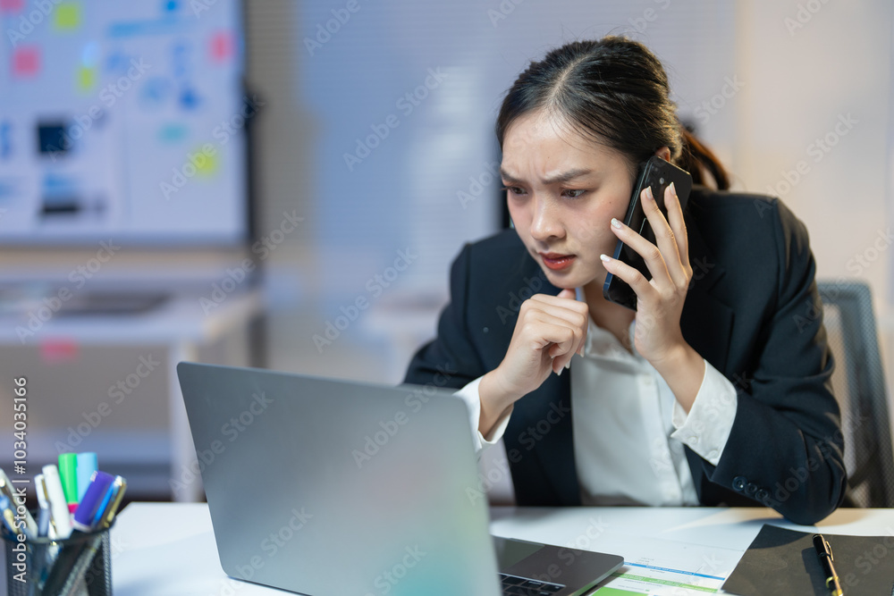Businesswoman is working late in the office. She is feeling stressed while having a phone conversation and looking at her laptop Businesswoman is working late in the office. She is feeling stressed while having a phone conversation and looking at her laptop