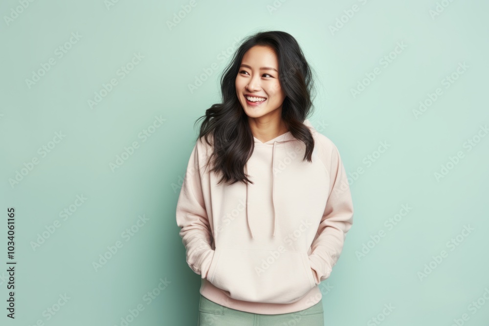 Portrait of a glad asian woman in her 30s dressed in a comfy fleece pullover while standing against pastel or soft colors background Portrait of a glad asian woman in her 30s dressed in a comfy fleece pullover while standing against pastel or soft colors background