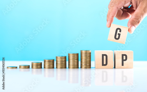 Hand holding a wooden block labeled 'GDP,' with a stack of coins placed on a table. Symbolizes economic growth, highlighting the role of Gross Domestic Product in measuring financial prosperity