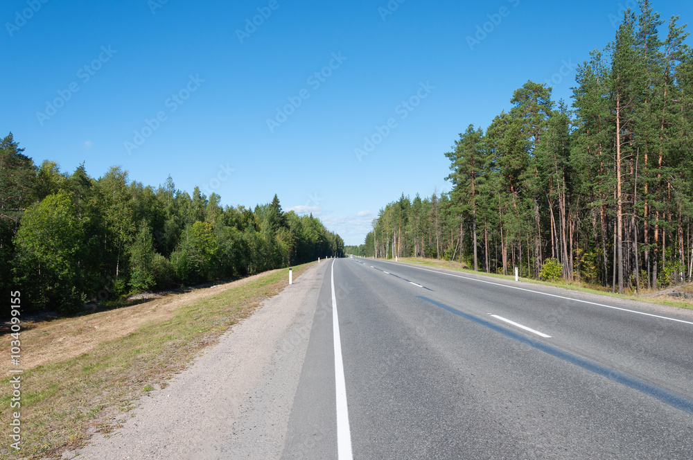 Asphalt highway through the forest in Karelia, blue sky, sunny summer day Asphalt highway through the forest in Karelia, blue sky, sunny summer day