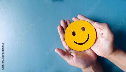 hand with smiley,Hands holding a blue smiley face cutout against a blue background, symbolizing happiness, positivity, and kindness. The simple and bright design conveys a message of joy and optimism