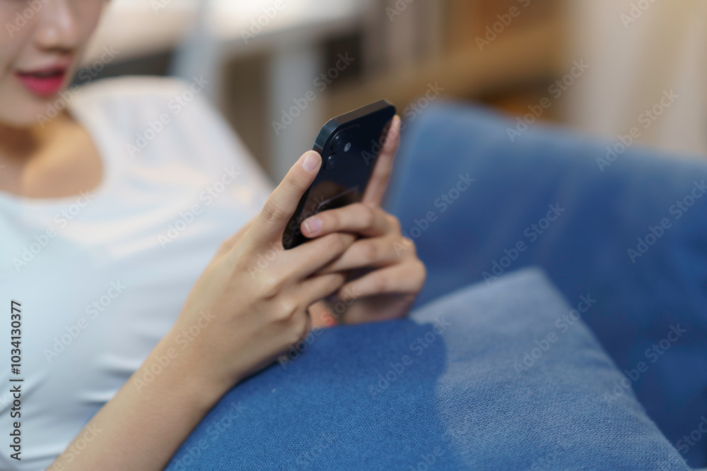 Young woman is lying on a blue couch using a smartphone, browsing social media Young woman is lying on a blue couch using a smartphone, browsing social media