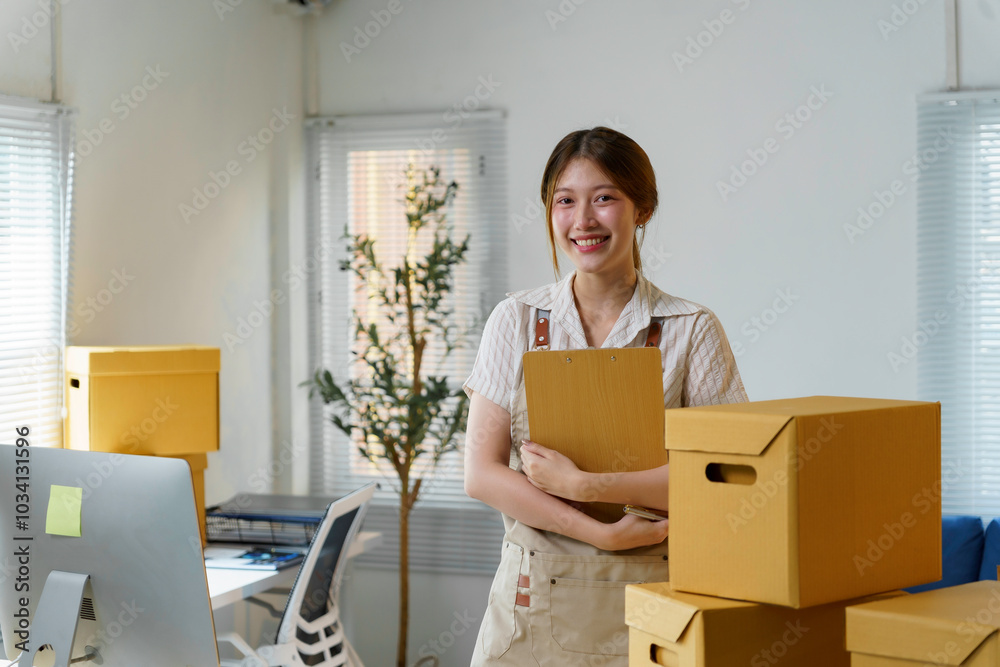 Asian sme business owner is smiling and holding a clipboard while standing in a warehouse full of cardboard boxes Asian sme business owner is smiling and holding a clipboard while standing in a warehouse full of cardboard boxes