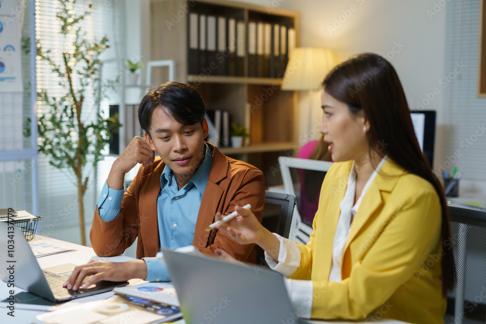 Two asian businesspeople working together, using a laptop, brainstorming and discussing ideas in a meeting Two asian businesspeople working together, using a laptop, brainstorming and discussing ideas in a meeting