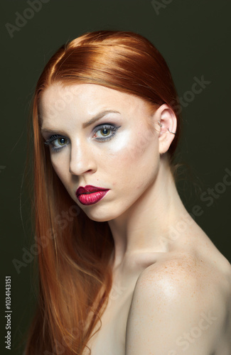 Woman with red hair and red lipstick poses for a photo. She has thick, beautiful hair. Fashion and beauty concept.