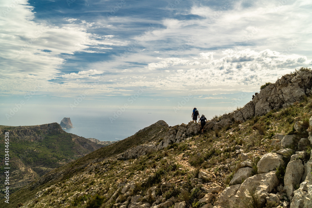 Silhouette of two hikers walking on a hill, against a cloudy sky, backlit. Silhouette of two hikers walking on a hill, against a cloudy sky, backlit.
