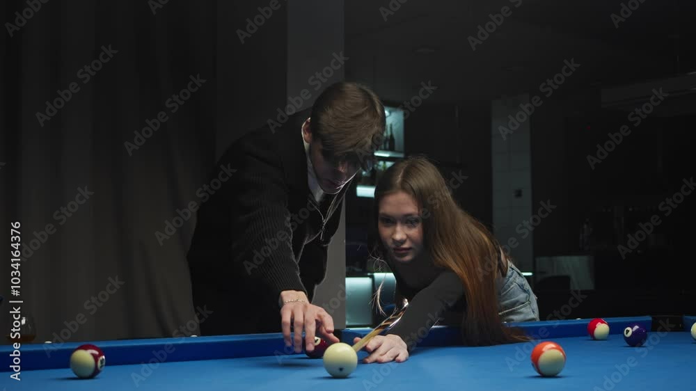 a young man teaches his girlfriend to play billiards. He explains the rules of the American pool game and guides her cue