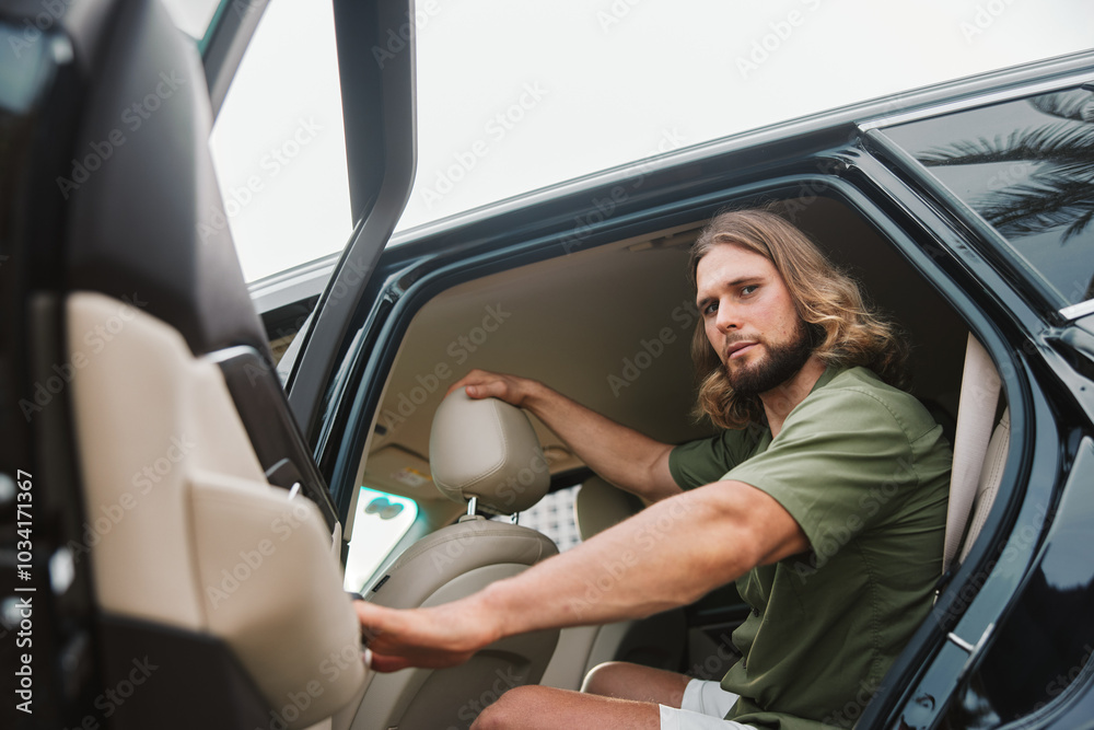 Stylish man getting into a black car with palm trees in the background Stylish man getting into a black car with palm trees in the background