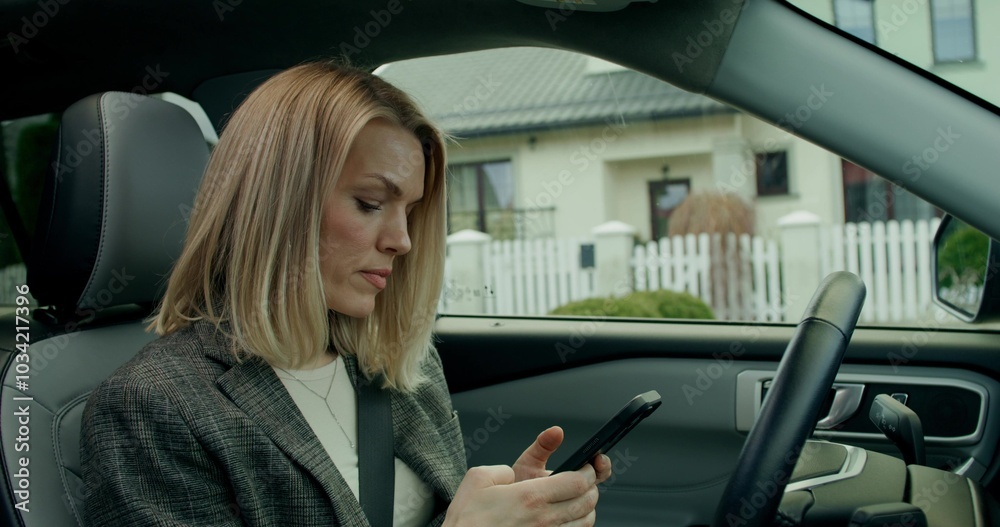 A stylish woman uses a mobile phone sitting in the driver's seat of a car while parking A stylish woman uses a mobile phone sitting in the driver's seat of a car while parking