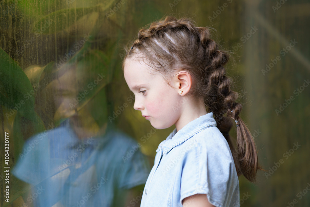 Little sad girl with two big pigtails near the glass. Concept of sad childhood Little sad girl with two big pigtails near the glass. Concept of sad childhood