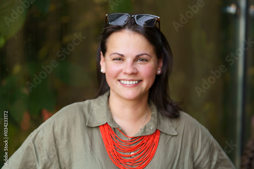 Beautiful dark-haired European woman in her thirties poses for a portrait photo in a khaki linen shirt and coral beads. Concept of natural female beauty