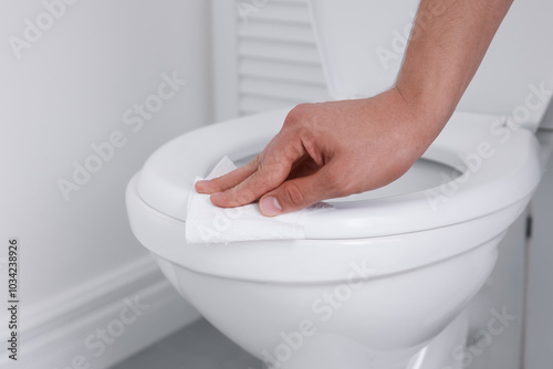 Man wiping toilet seat with paper in bathroom, closeup