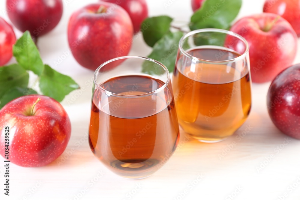 Fresh apple juice in glasses, fruits and green leaves on white table, closeup Fresh apple juice in glasses, fruits and green leaves on white table, closeup