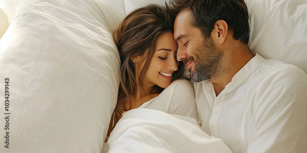 Young loving couple cuddling in bed in the morning. Young man and woman hugging laying on white sheets. Husband and wife in love.