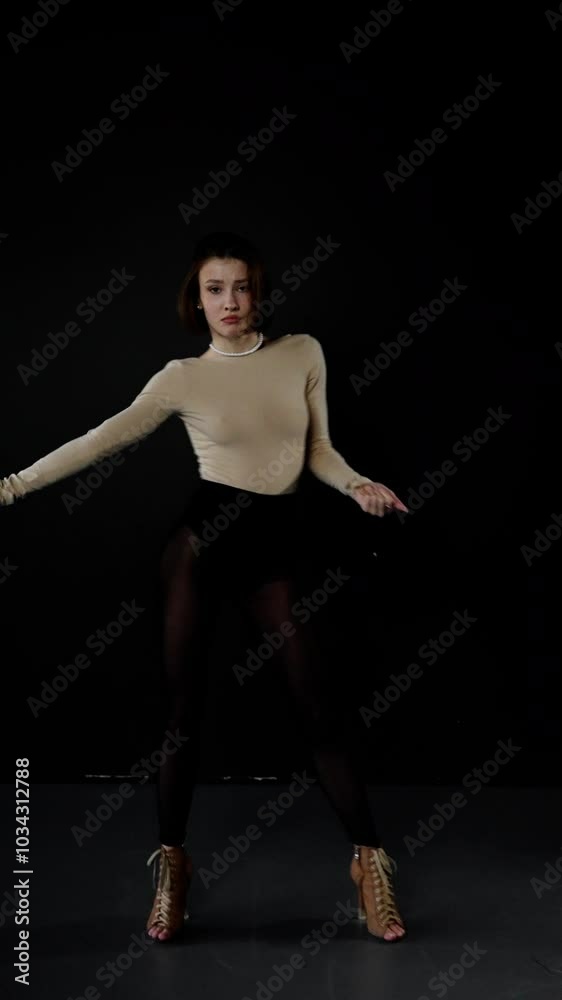 Young woman in a beige leotard and black tights performs a contemporary dance routine on a minimalist stage featuring a solid black backdrop Young woman in a beige leotard and black tights performs a contemporary dance routine on a minimalist stage featuring a solid black backdrop