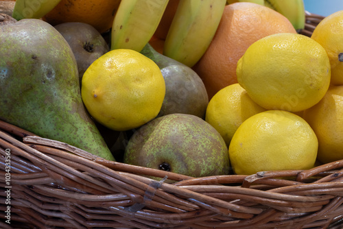 Fresh ripe pears, lemons, oranges and bananas in a wicker wooden basket close-up