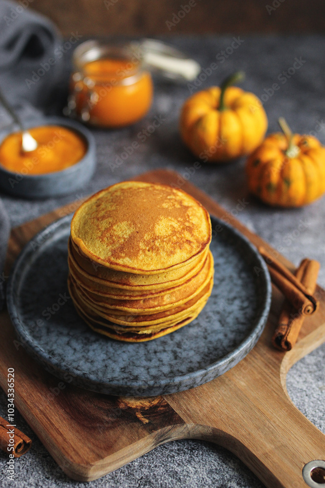 Light and fluffy pumpkin pancakes with honey and walnuts on a blue plate. Wooden cutting board, pumpkin pure in a glass jar, cinnamon sticks, and dark background. Light and fluffy pumpkin pancakes with honey and walnuts on a blue plate. Wooden cutting board, pumpkin pure in a glass jar, cinnamon sticks, and dark background.