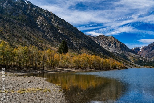 Scenic view of a mountain range with autumn aspen trees and a lake under a blue sky. Sierra Nevada