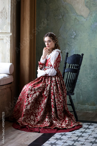 Photography Young woman in historic renaissance dress with curled hairstyle sitting in old room with antique interior