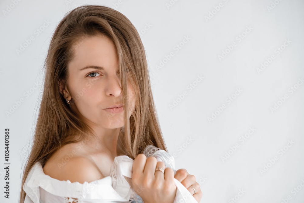 Pretty 30s woman looking at camera in white top shirt exposing shoulder. Studio portrait. Boho style dress. Natural beauty face. Concept of tenderness and femininity. Flirting look Pretty 30s woman looking at camera in white top shirt exposing shoulder. Studio portrait. Boho style dress. Natural beauty face. Concept of tenderness and femininity. Flirting look