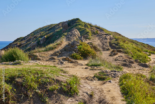 Landscape of a grassy hill dotted with rugged, weathered boulders under a clear blue sky