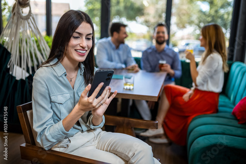 Woman using her phone in the restaurant. Her friends are in the background.